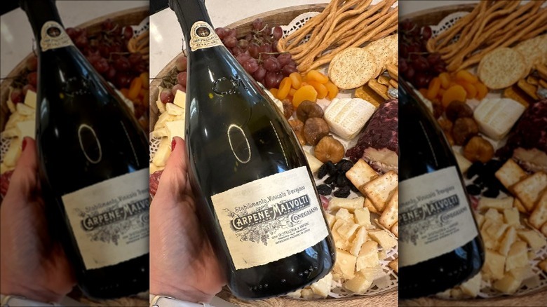 holding carpene malvoti prosecco over cheese and charcuterie board