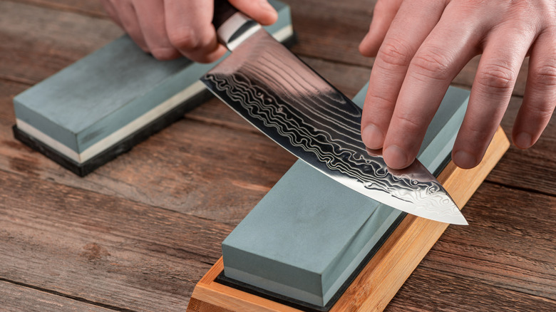 hands sharpening knife against whetstone