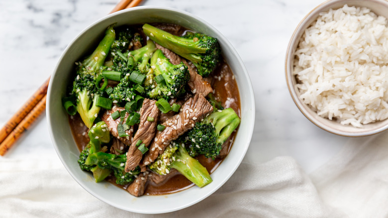 beef & broccoli bowl next to rice bowl and chopsticks