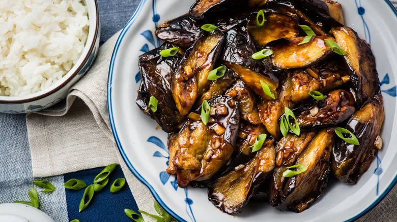 plate of eggplant in brown sauce by rice bowl