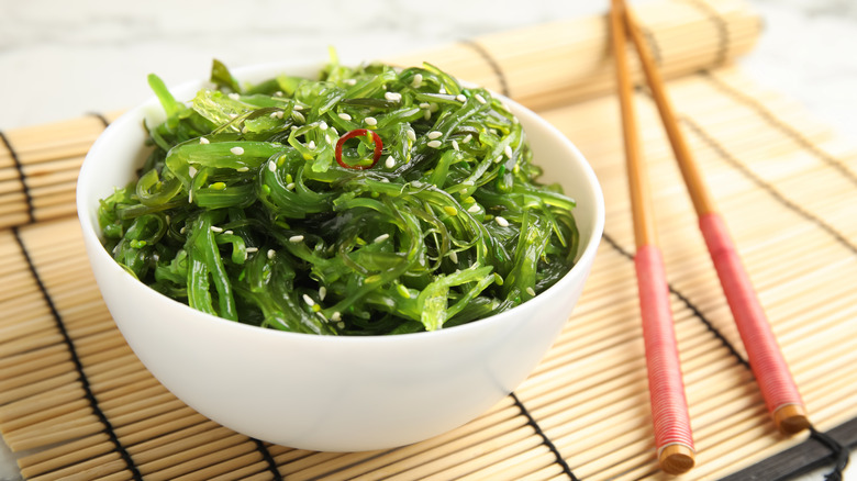 bowl of seaweed salad and chopsticks on bamboo mat 