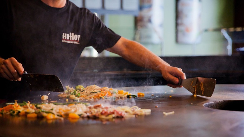 HuHot employee cooking on large flat grill