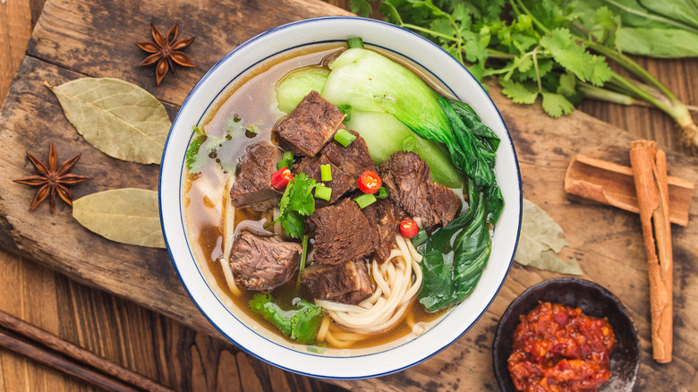 bowl of beef noodle soup displayed on wooden board