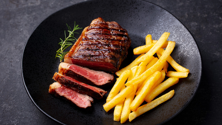 Steak frites on a black plate against a dark background