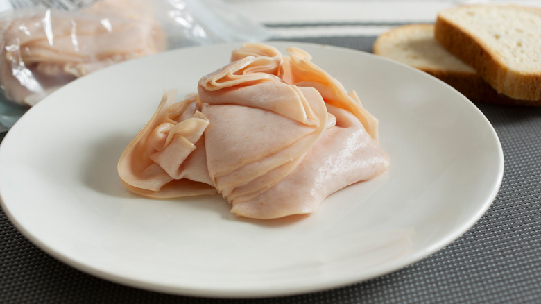 Sliced deli turkey on white plate with bread and plastic bag in background