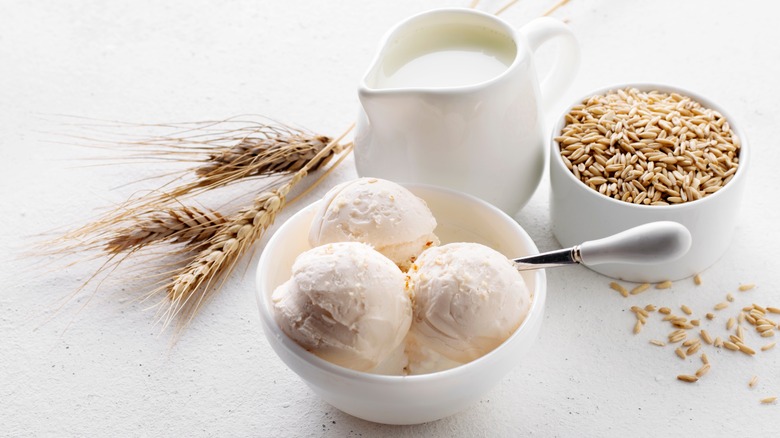 Three scoops of oat milk ice cream in a bowl with jug of oat milk and dish filled with oats