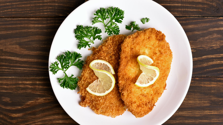 Plate of two breaded chicken cutlets with lemon and garnish