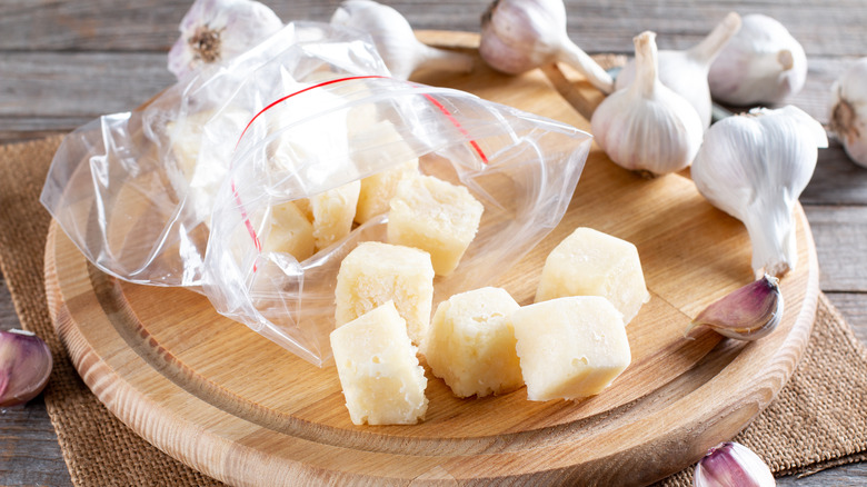 Frozen minced garlic cubes coming out of bag on wooden board