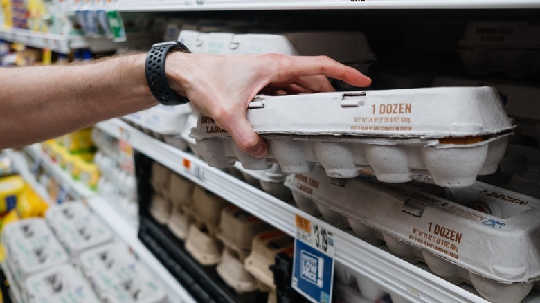 hand grabbing egg carton from grocery shelves