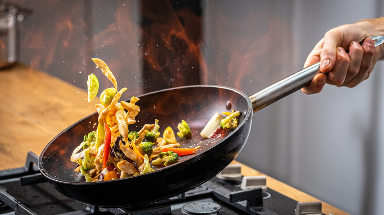 Chef tosses food in a pan over the stove