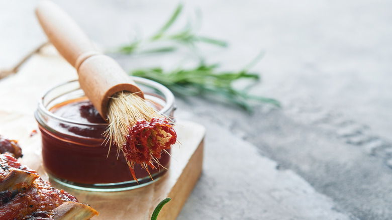 A brush lies on top of a container of barbecue sauce