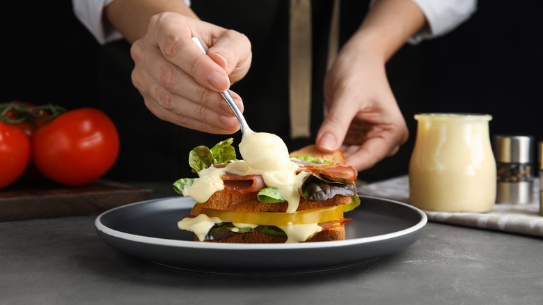 Spoon spreading mayonnaise on a meat and veggie sandwich