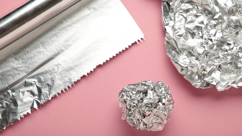 Aluminum foil roll and balls on pink background