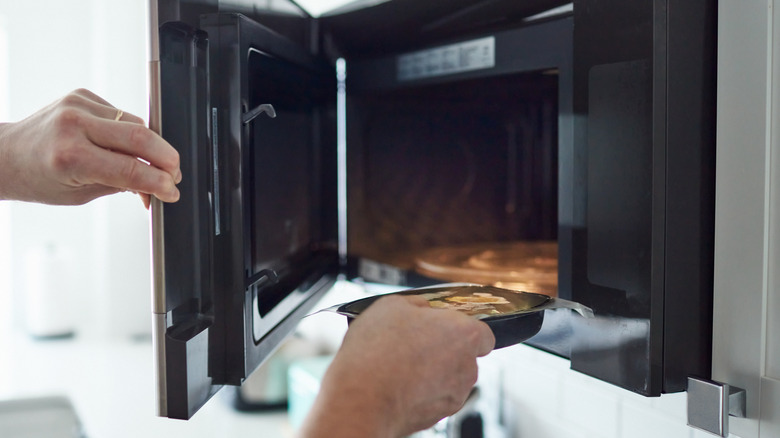 Person putting frozen dinner into microwave