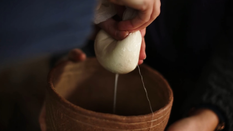 Hand squeezing cheese curd to separate whey into clay bowl