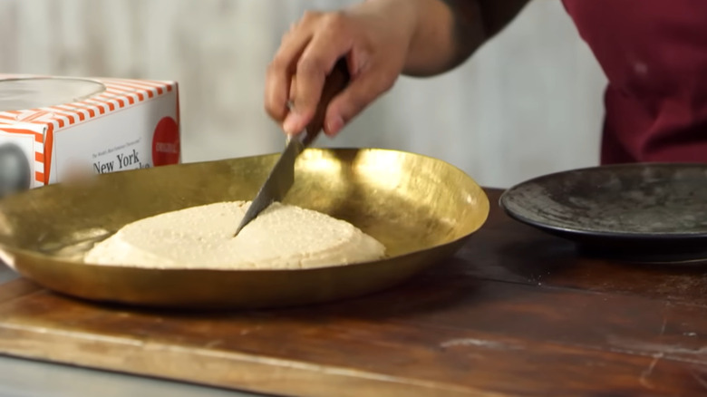 hand cutting into ancient greek style cheesecake in gold colored bowl