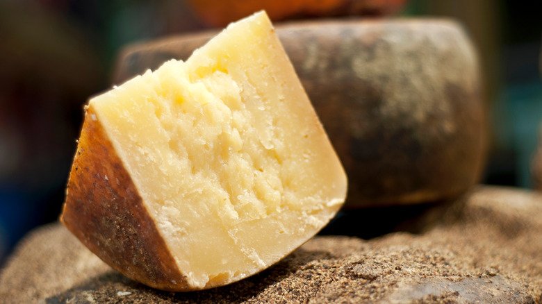 A wedge of Pecorino Romano sits on top an uncut wheel of cheese