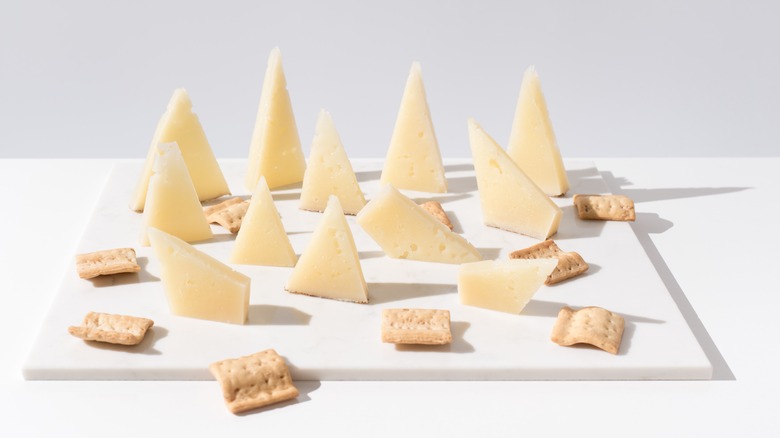 Triangles of pale yellow cheese on white background with crackers of white cutting board