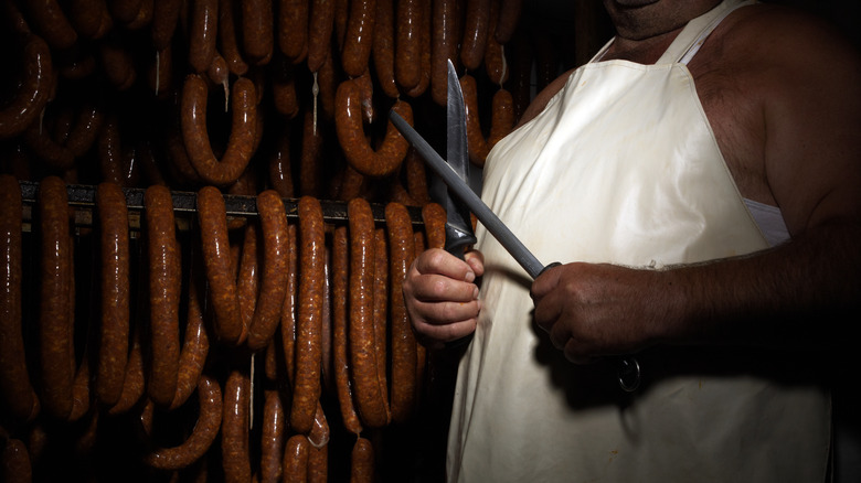 butcher with knives in front of sausages