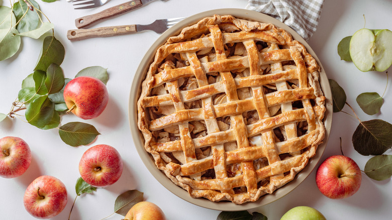 A freshly bked apple pie with latticed pastry top, and apples scattered about