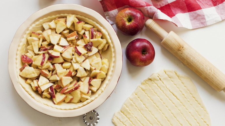 unbaked apple pie dish filled with apples surrounded by apples and a lattice dough