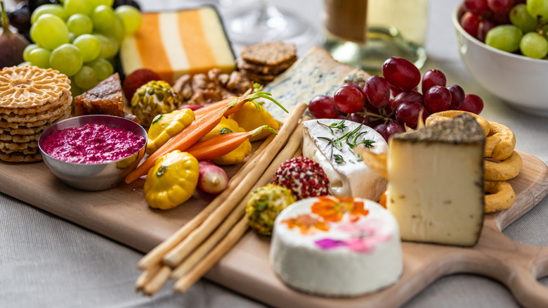 Close up of a cheese board with and assortment of fruit, crudité, and crackers