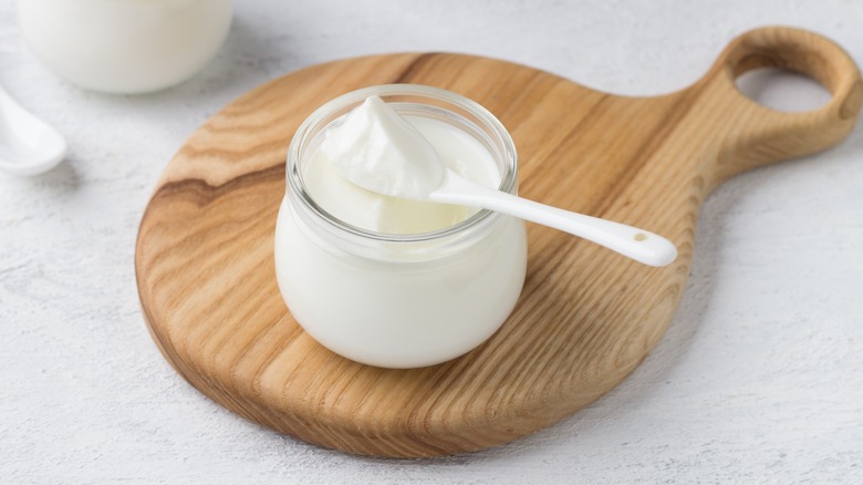 yogurt in a glass bowl on a wooden board on a light gray surface