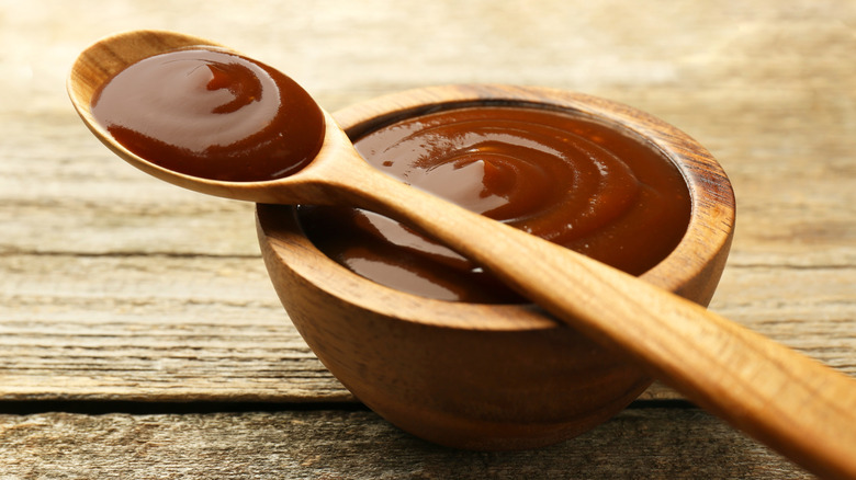 Barbecue sauce in wooden bowl and spoon balanced across the top