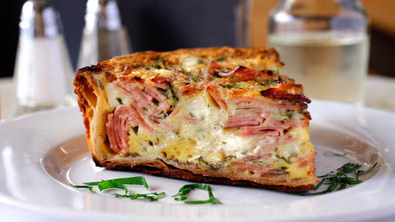 Slice of ham and cheese quiche on white plate