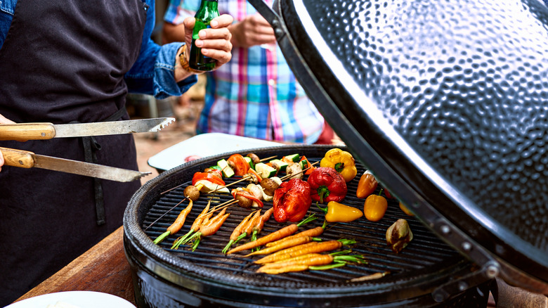 man stands over open grill cooking mixed veggies