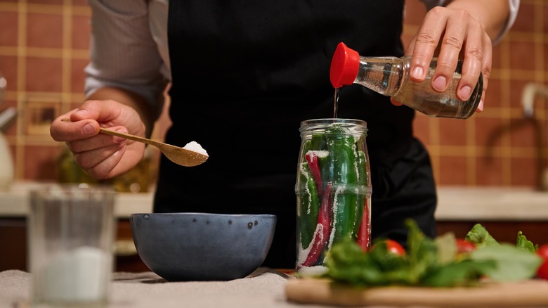 pouring vinegar over hot peppers in jar