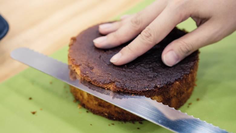 Person cutting cake layer with serrated knife