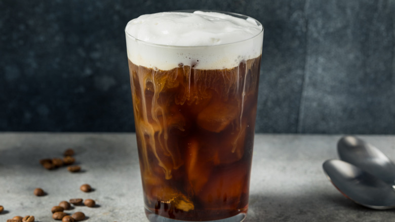 Iced coffee topped with foam in a glass