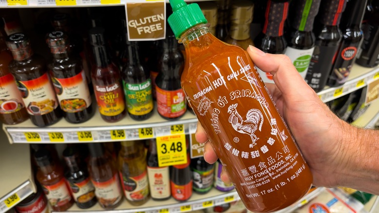 Man holding a bottle of sriracha sauce