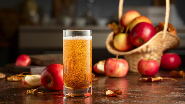 Glass of apple cider beside basket of fresh apples.