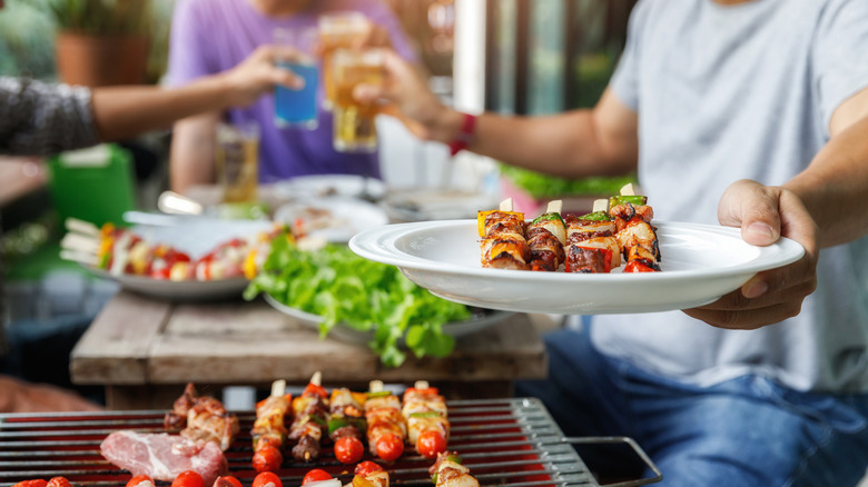 Person holding skewers and beer