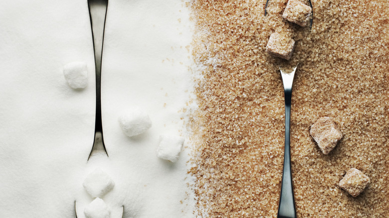 White and brown sugar spread out on table with spoons