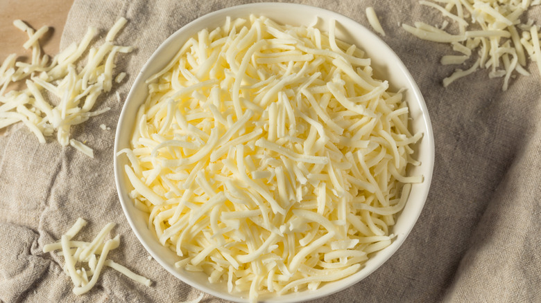 shredded mozzarella cheese in a bowl on a cloth from above