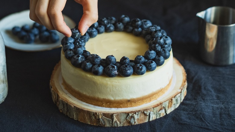 Fingers putting blueberries on cheesecake