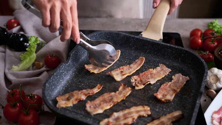 Hand holding tongs flipping bacon