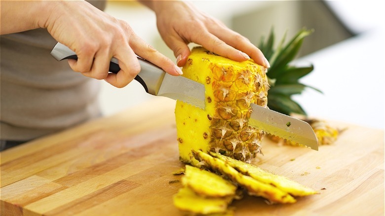 Hands cutting off pineapple skin 
