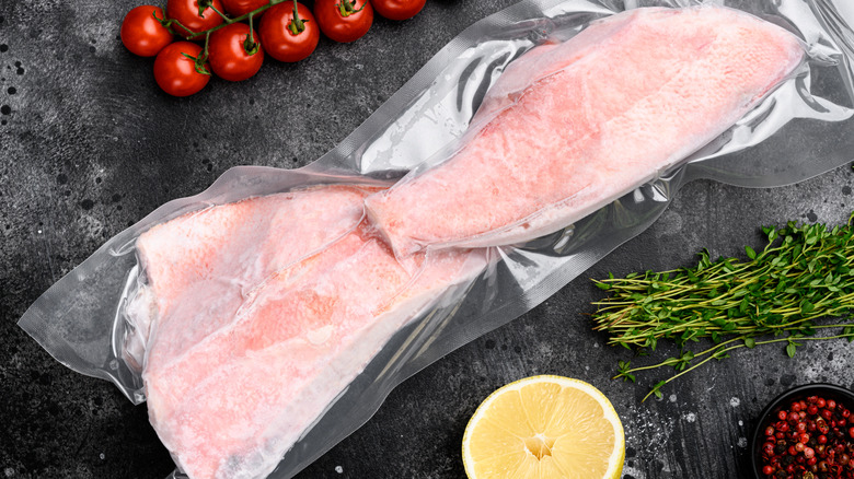 Two frozen fish filets in air-tight bags next to fresh ingredients on a counter