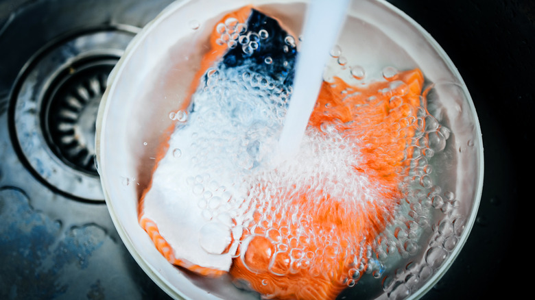 Frozen salmon defrosting under water in stainless steel bowl