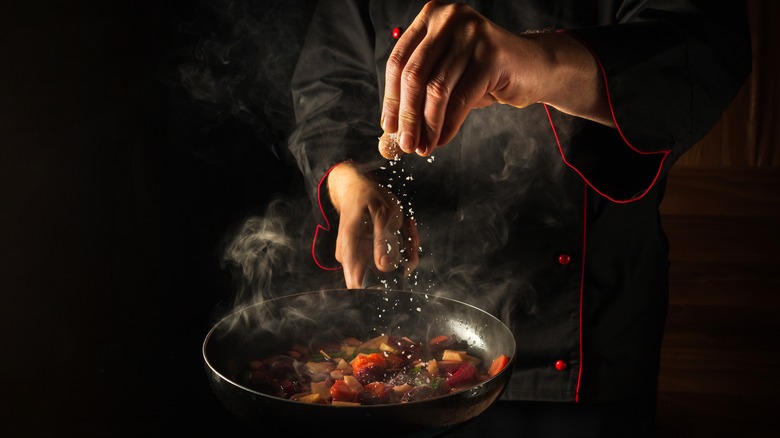 Chef salting vegetables in skillet