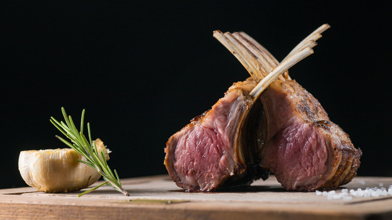 Rack of lamb on cutting board with garlic and rosemary