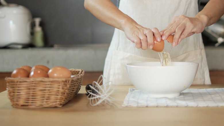 Two hands cracking an egg into a bowl