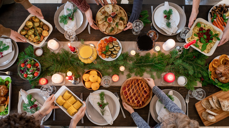 A Christmas potluck dinner with people setting different dishes on a festive table