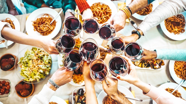 Group clinks red wine glasses over bowls of pasta