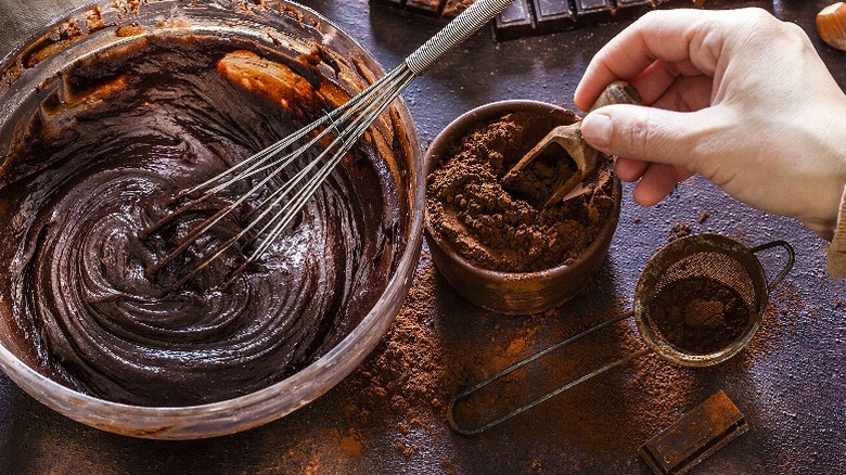 man adding cocoa powder to a bowl of chocolate batter