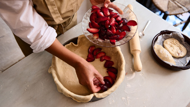 View from above of a person arranging fresh plums inside of a raw pie crust